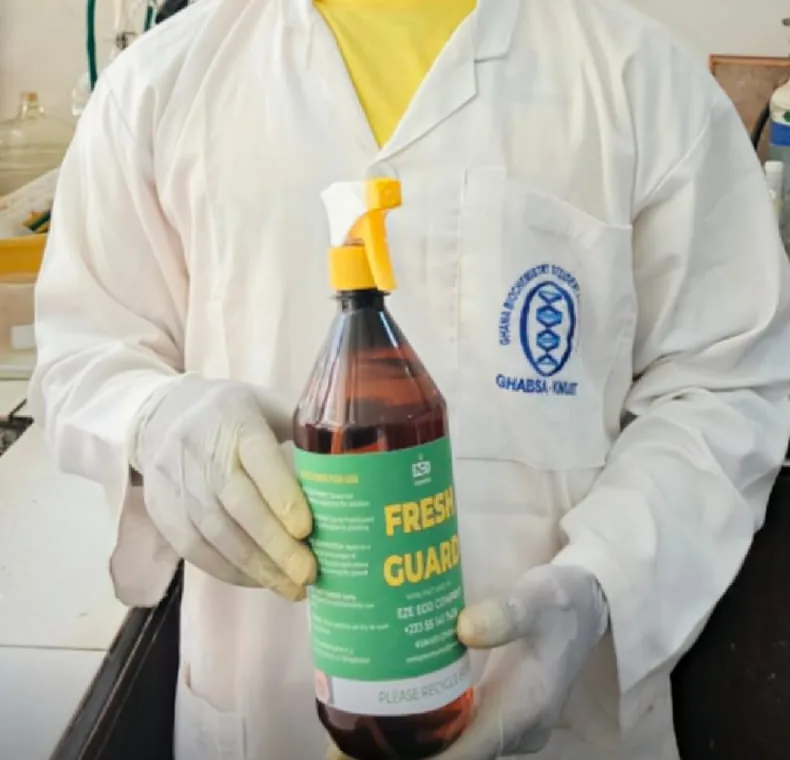 A researcher in a lab coat and gloves holding up a FreshGuard spray bottle in the laboratory